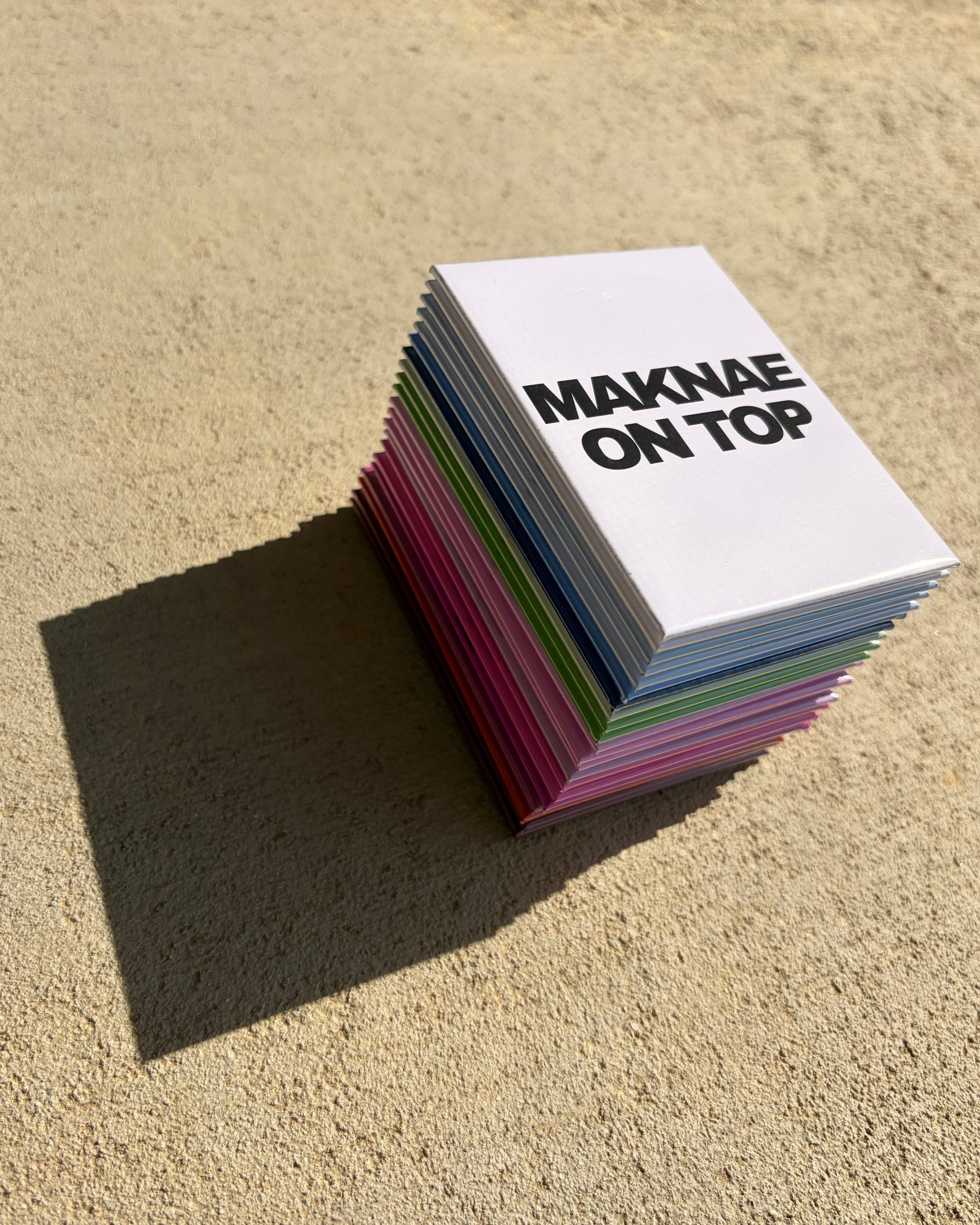 Stack of colorful magnets with 'MAKNAE ON TOP' text on a textured surface