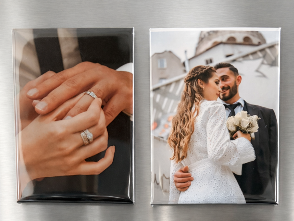 Two photo magnets on a metallic surface, one showing hands with rings and the other a couple embracing.